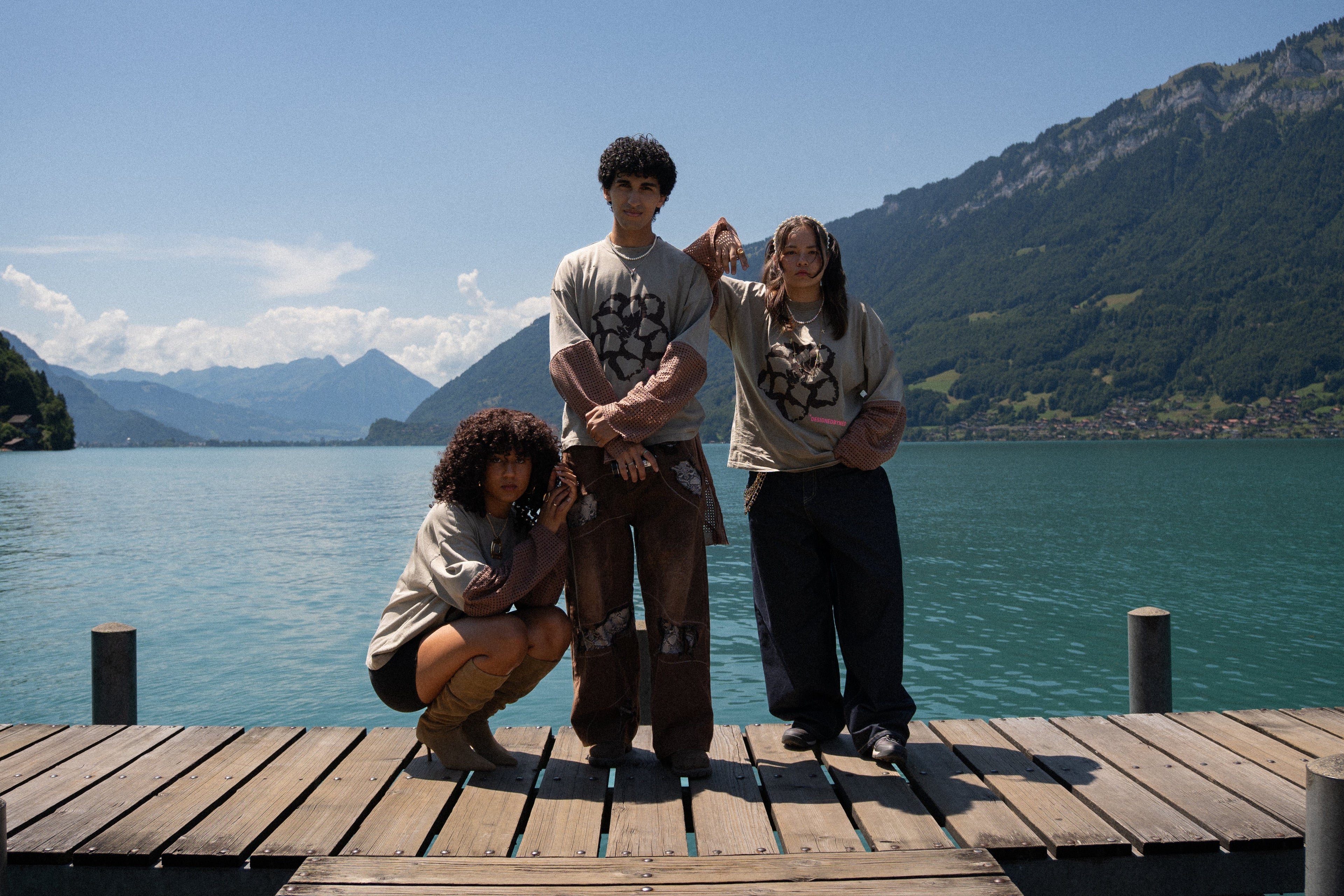 Three people posing on a wooden dock by a lake with mountains in the background